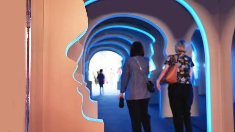 Visitors exploring head profile arches in a glowing blue light art exhibition Stock Photos