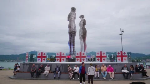 Visitors rest beneath iron figures monument on waterfront promenade 動画素材 341852137