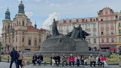 Visitors sit and relax beside the Jan Hus Memorial in Prague Old Town Square Stock Footage 342342166