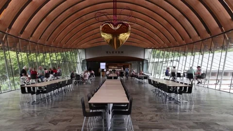 Visitors sit in a large cafeteria under a giant golden heart sculpture. Stock Footage 345618822