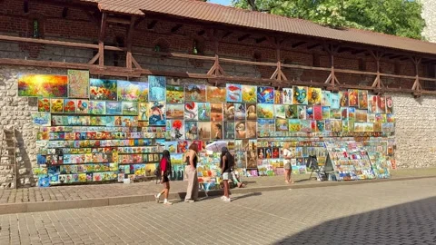 Visitors stop to look at colourful paintings displayed along the medieval walls Stock Footage 337796513