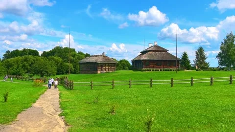 Visitors walk along a path in a historic village with wooden houses and green fi Stock Footage 326375600