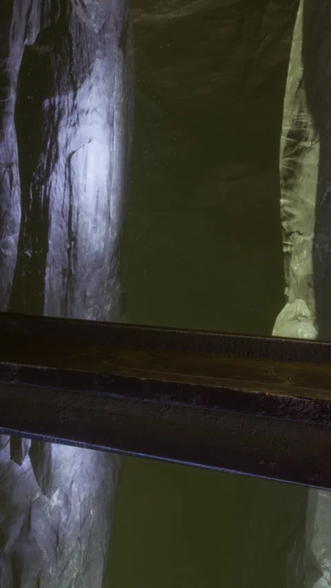 Visitors walk along wooden path inside a dark cave near water source in evening Stock Footage 334185378