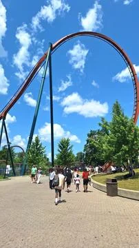Visitors walk beneath a large roller coaster loop track. Stock Photos