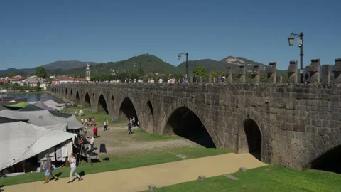 Visitors walk beneath the Roman bridge arches in Ponte de Lima Stock Footage 346134199