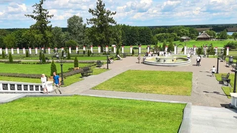 Visitors walk through a large park with grass, flowers, and a fountain on a sunn Stock Footage 325329175