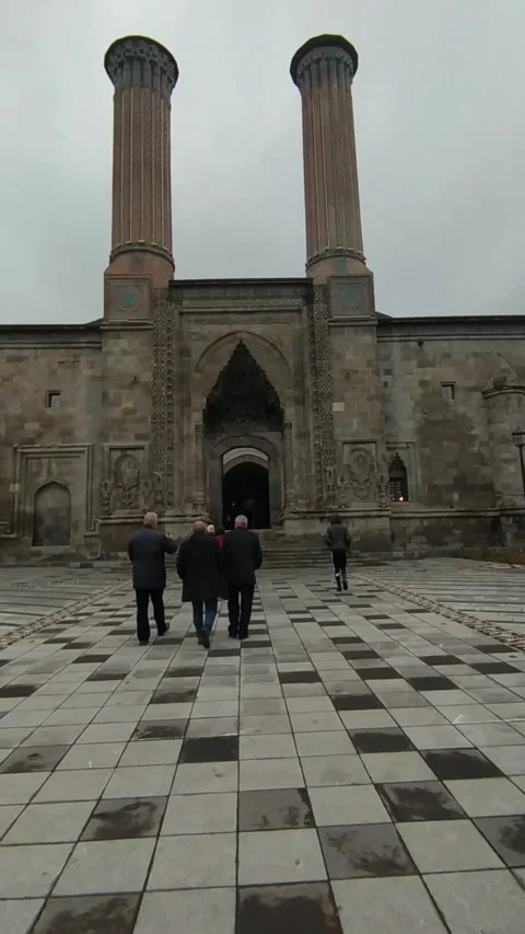 Visitors walking in front of the Twin Minaret Madrasa in Erzurum. vertical shot Stock Footage 239845963