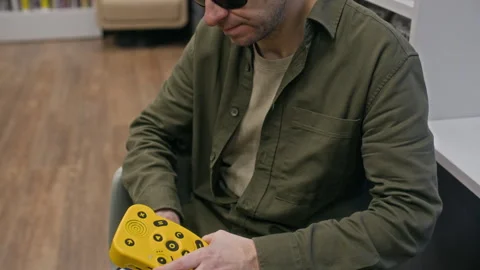 Visually Impaired Man Using Digital Talking Book Player in Accessible Library Stock Footage 327454309