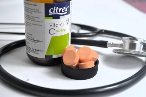 A Vitamin C bottle with tablets on cap beside stethoscope Stock Photos