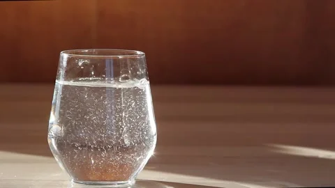 A vitamin C tablet is thrown into a transparent glass glass with water. Stock Footage 142758758