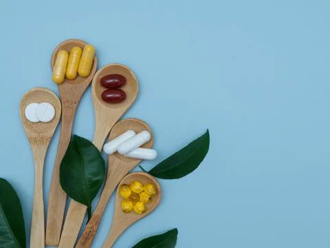 Vitamin D, B, E, omega 3, zinc on wooden spoons decorated with green leaves on a Stock Photos