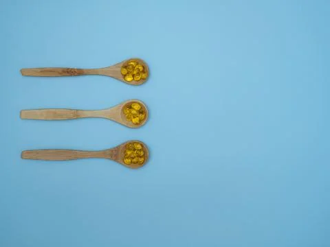 Vitamin D, E or fish oil capsules in wooden spoons on blue background with copy Stock Photos