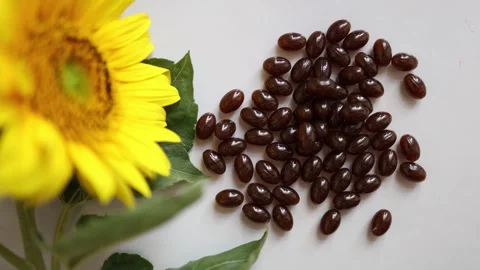 Vitamin E softgel capsules beside bright sunflower on white background Vidéo 344043974