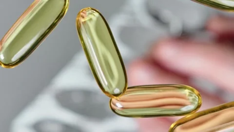 Vitamine E, fish oil capsules spill out of a blister pack Stock Footage 267421019
