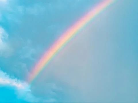 Vivid Diagonal Rainbow Arc Against Clear Blue Sky with Clouds Stock Photos