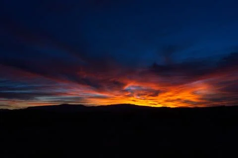 Vivid orange clouds at sunset over a mountain range. Stock Photos