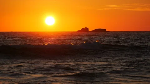Vivid, orange sky at sunset over the ocean as waves form on water Stock Footage 110620283