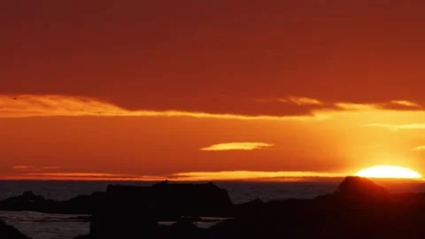 Vivid orange sunset over the ocean with silhouetted rocks and dramatic clouds. Stock Footage 327260192