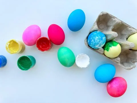 Vividly painted Easter eggs scattered beside open cans of colorful paint and an Stock Photos