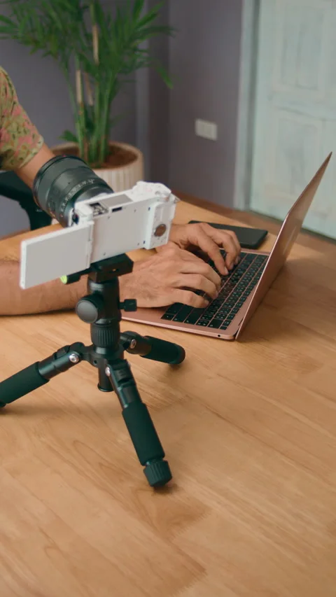 A vlogger is seen setting up a camera while working on a laptop at their home or Stock Footage 276341564