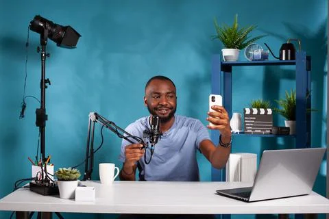 Vlogger sitting in vlogging studio holding microphone taking a selfie with Stock Photos