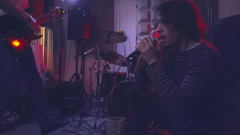 The vocalist sings while sitting on the floor next to the guitarist and drummer. Video stock 256291262