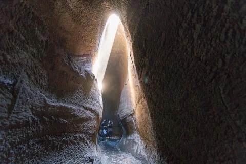 Volcanic cave interior with light beam and visitors Photos