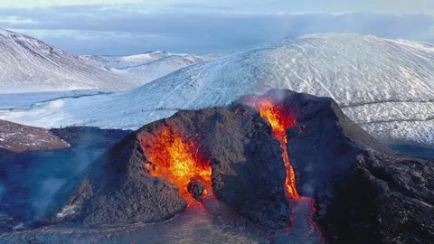 Volcanic eruption spewing molten lava from crater with snowy icelandic mountains Stock Footage 345484645