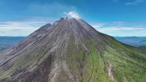 The volcano rises like a rugged stone pyramid above a patchwork of green meadows Stock Footage 328206871
