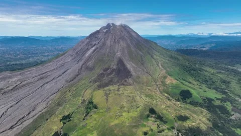 The volcano rises like a rugged stone pyramid above a patchwork of green meadows Stock Footage 328486753