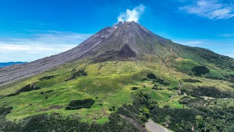 The volcano rugged slopes tower above rolling hills, black lava scars slicing Stock Photos