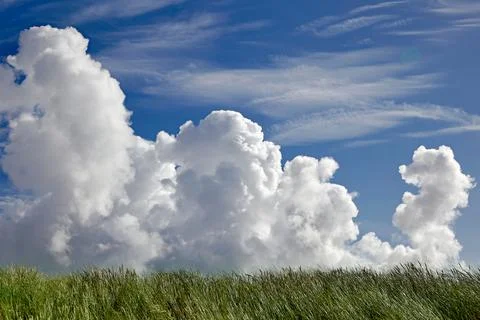 Volumetric clouds in the blue sky and green field grass Stock Photos