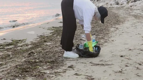 Volunteer cleaning plastic trash on a polluted beach, picking up bottles and Vidéo 327337643