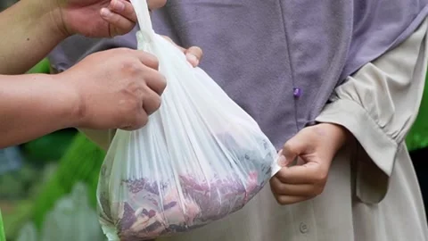 A volunteer handing over a white plastic bag filled with raw sacrificial meat Video stock 338046938