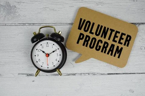 Volunteer Program text with alarm clock on wooden background Stock Photos