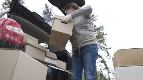 A volunteer in a protective suit loads boxes into the trunk of a car Video stock 149247994