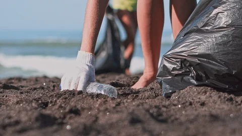 The volunteer raises and throws a plastic bottle into the bag on the beach Stock Footage 95277004