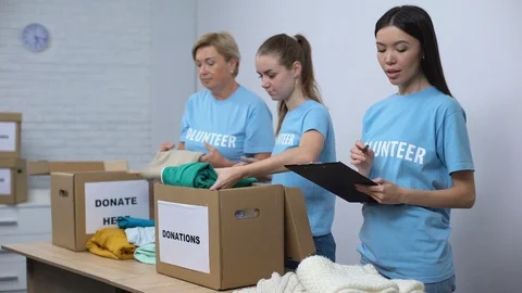 Volunteers putting clothes in donation boxes, smiling social worker making notes Stock Footage 113394617