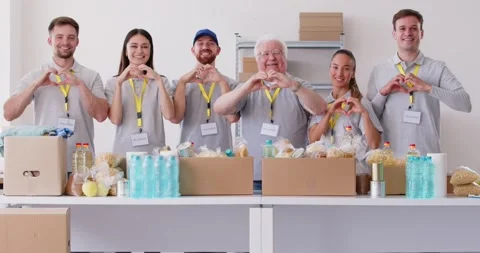 Volunteers stand in front of table full of collected food items, making heart Vídeo Stock 308664469