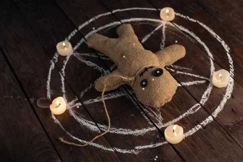 Voodoo doll on a wooden background with dramatic lighting and candles. The co Stock Photos