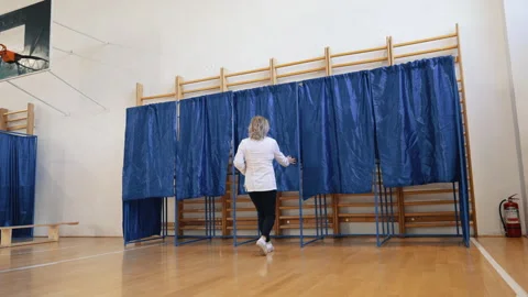 A voter stepping into the blue-curtained booth to cast their vote Stock Footage 320962711