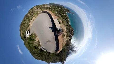 VR360 effect A man stays on a road overlookking the sea in a sunny evening Stock Footage 107192406