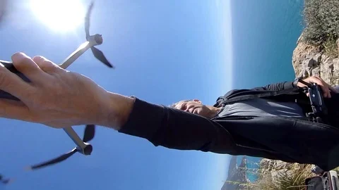 VR360 effect Vertical A man do a take off with a drone on a high cliff on sea Stock Footage 107444601