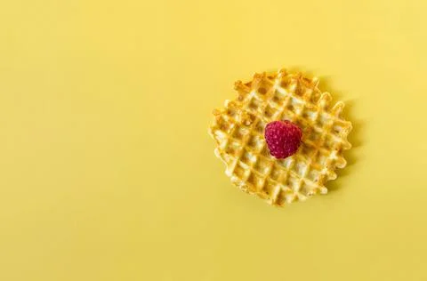 Waffle with a large raspberry berry on a yellow background of kopi space. Stock Photos