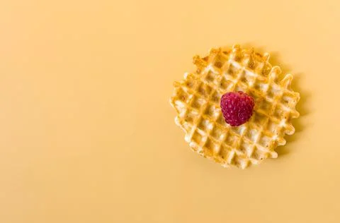 Waffle with a large raspberry berry on a yellow background of kopi space. Stock Photos