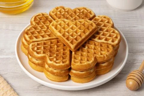 Waffles made in a heart shape served on a plate with honey and syrup nearby Stock Photos