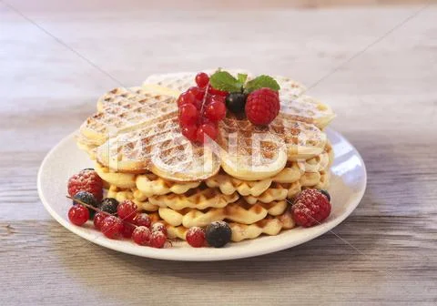 Waffles with raspberries, blueberries and redcurrants on a wooden plate Stock Photos