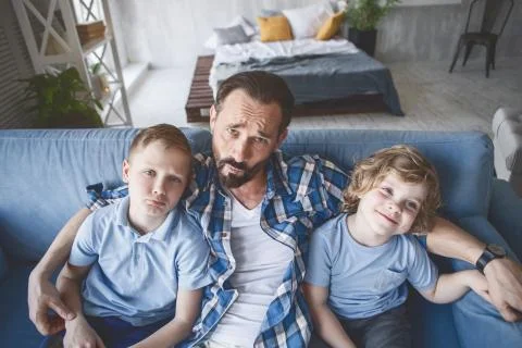 Wailful dad hugging kids on couch Stock Photos