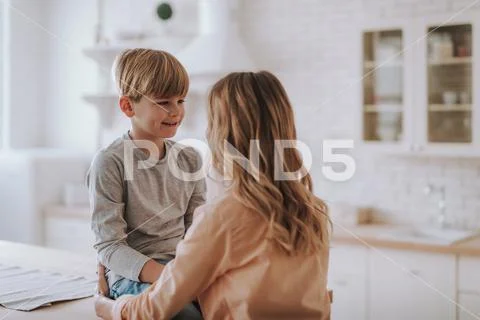 Waist up of cheerful boy smiling to his mother in the kitchen Stock Photos