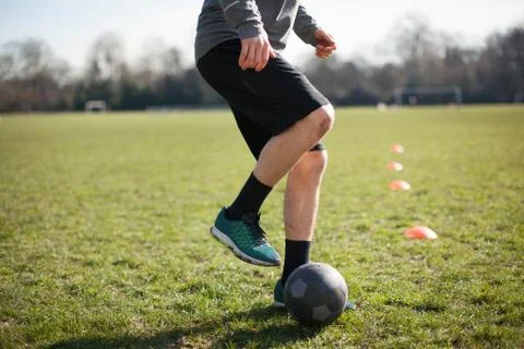 Waist down of young man practicing soccer on playing field Stock Photos